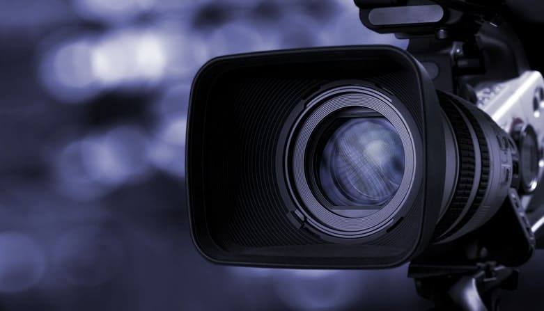 Close-up of a professional video camera lens, capturing intricate details and reflections that are vital across various industries, set against a blurred background.