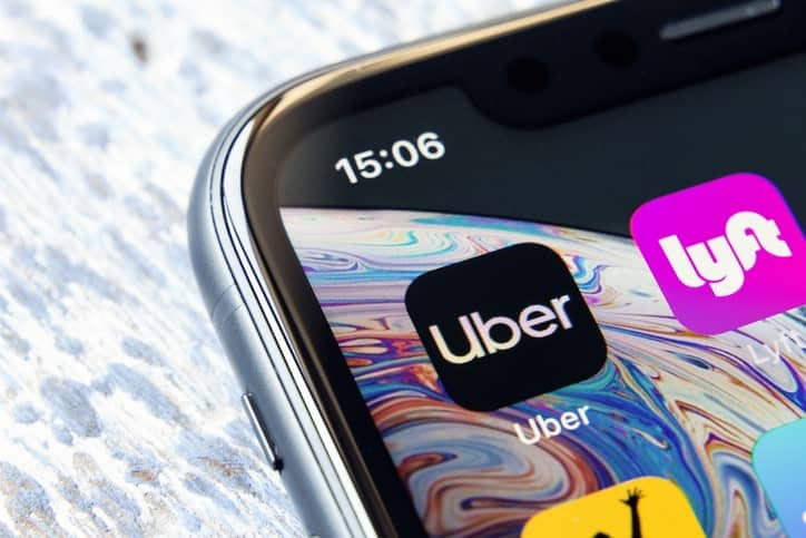 A close-up of a smartphone screen showcases the Uber and Lyft app icons, representing leaders in the ride-sharing industry, with the time displayed as 15:06.