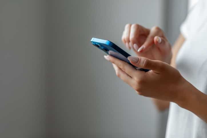 A person is deeply engrossed in their smartphone, using both hands and focusing intently on the screen, perhaps exploring the latest trends in various industries.
