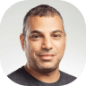 Portrait of a man with short hair and a neutral expression, wearing a dark T-shirt about to capture the essence of synergy, against a light gray background.